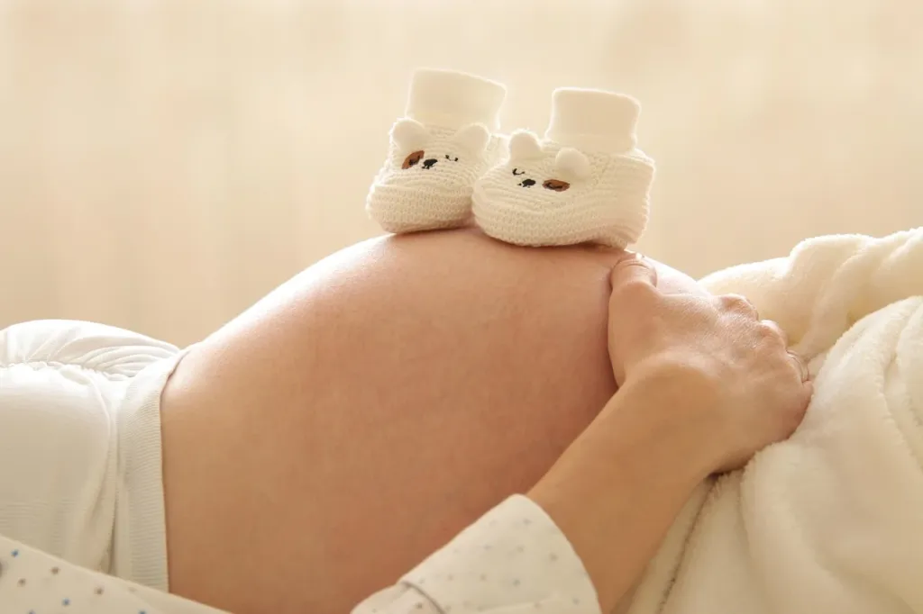Brzuch kobiety w 23. tygodniu ciąży obok wagi i miarki, symbolizujące monitorowanie prawidłowego przyrostu masy ciała.